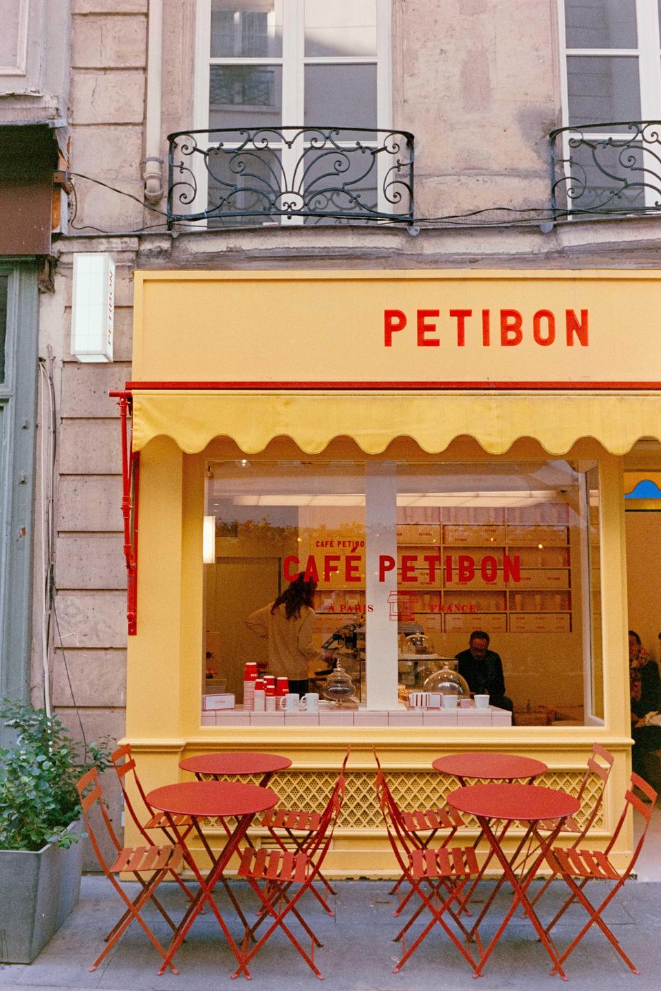A yellow cafe with red tables and chairs outside is visible from the street.