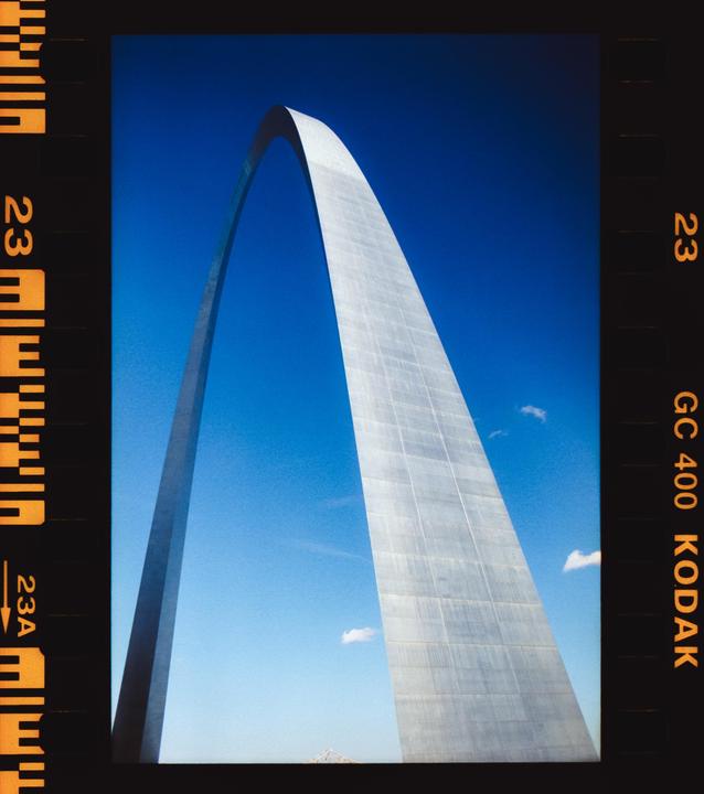 The Gateway Arch stands tall against a clear blue sky with a few small clouds.