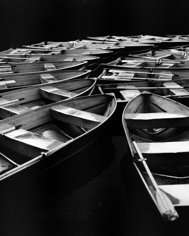 Numerous rowboats are docked closely together on a dark body of water.