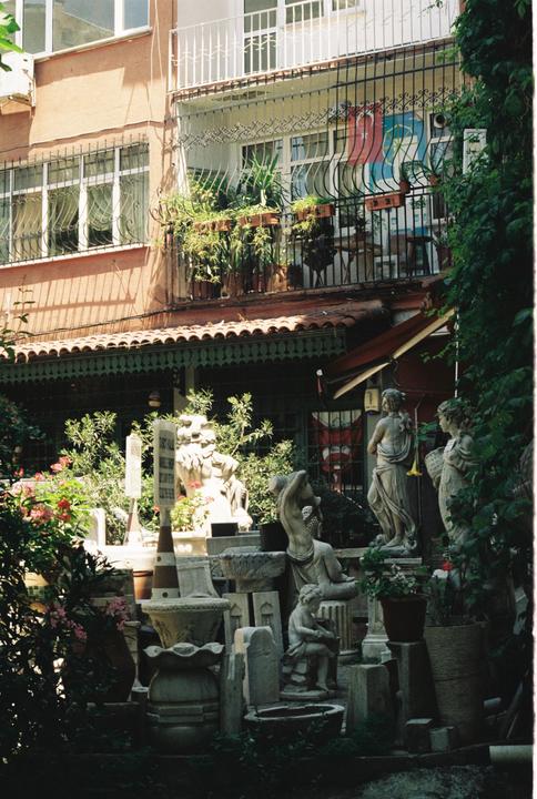 A collection of statues and planters are arranged in front of a building with balconies and lush greenery.