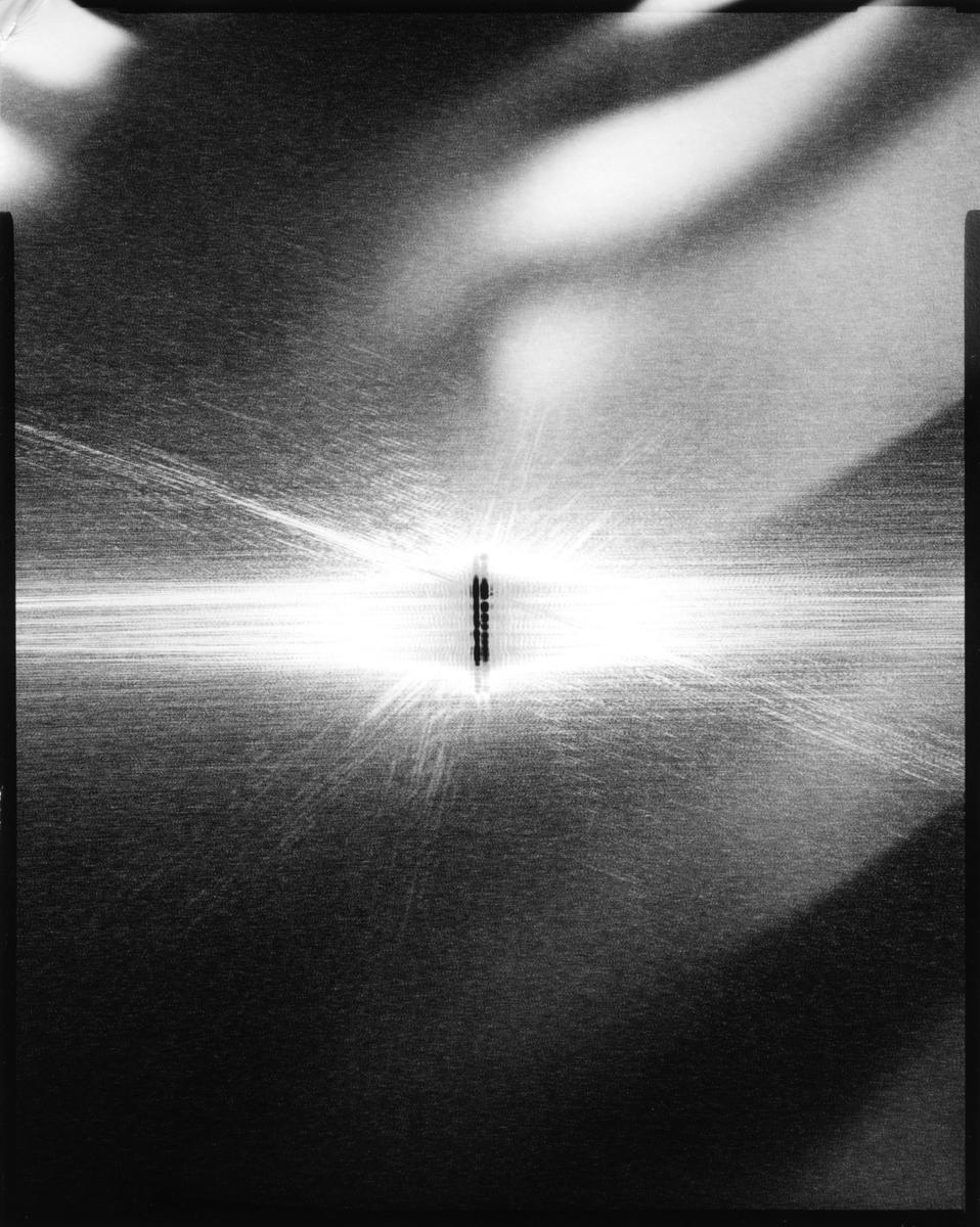 A bright light source shines through a double slit, creating an interference pattern on a surface.