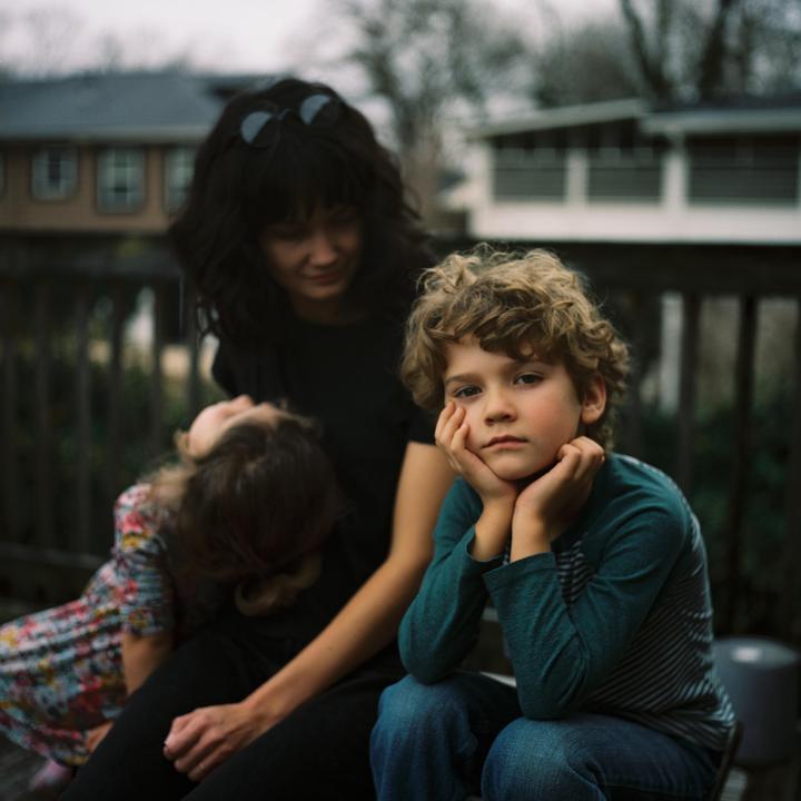 A woman and two children are sitting on a wooden deck outdoors.