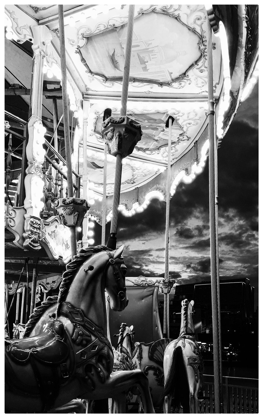 A carousel with horses is shown against a cloudy sky at dusk.