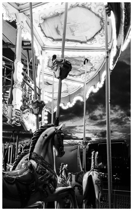 A carousel with horses is shown against a cloudy sky at dusk.