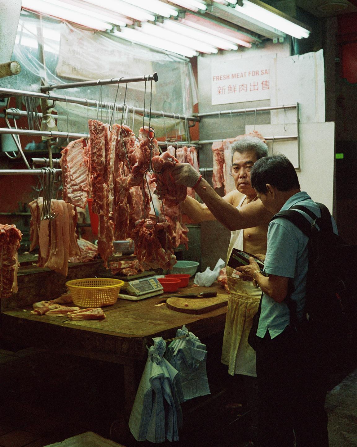 A man sells meat to a customer in a market stall in Hong Kong.