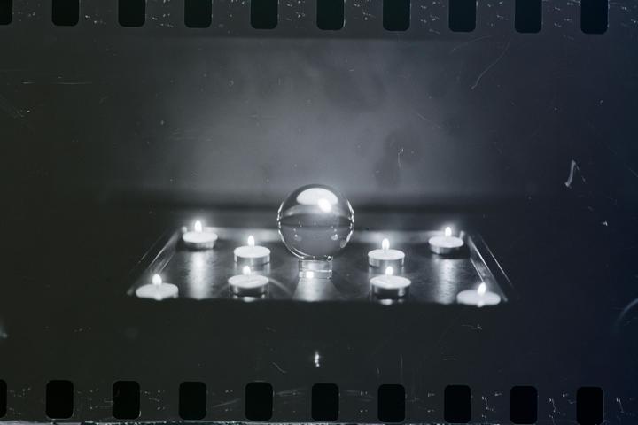A crystal ball is surrounded by lit tea light candles on a reflective surface.