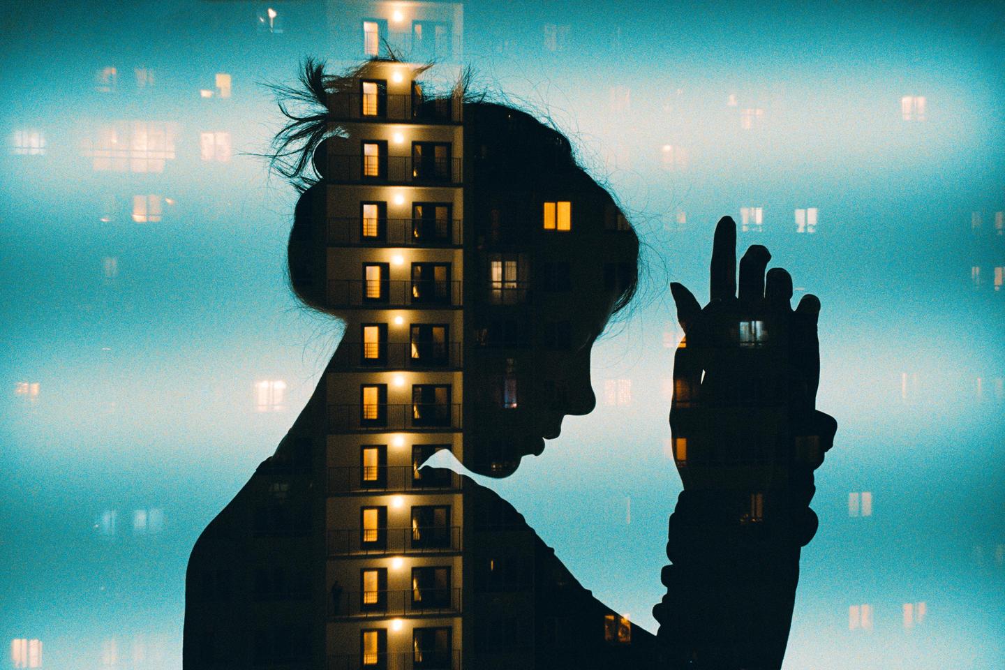 A double exposure shows the silhouette of a woman with a building superimposed over her form, against a blue sky with glowing windows.