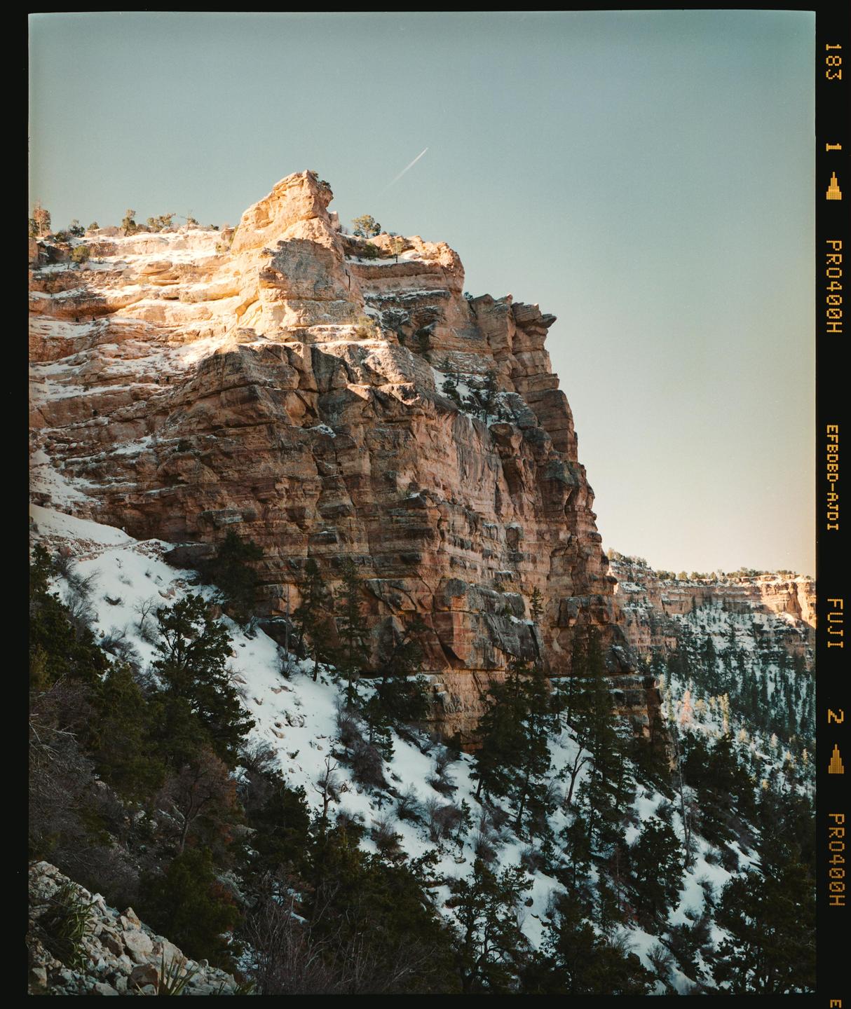 A snow-dusted mountain with pine trees is illuminated by the sun under a clear sky.
