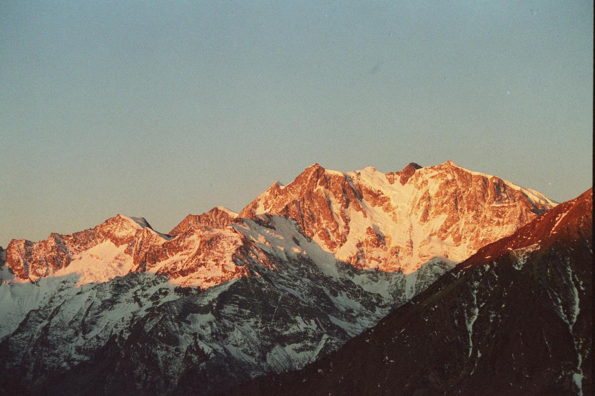 Snow-capped mountains are illuminated by the golden light of sunrise under a clear sky.