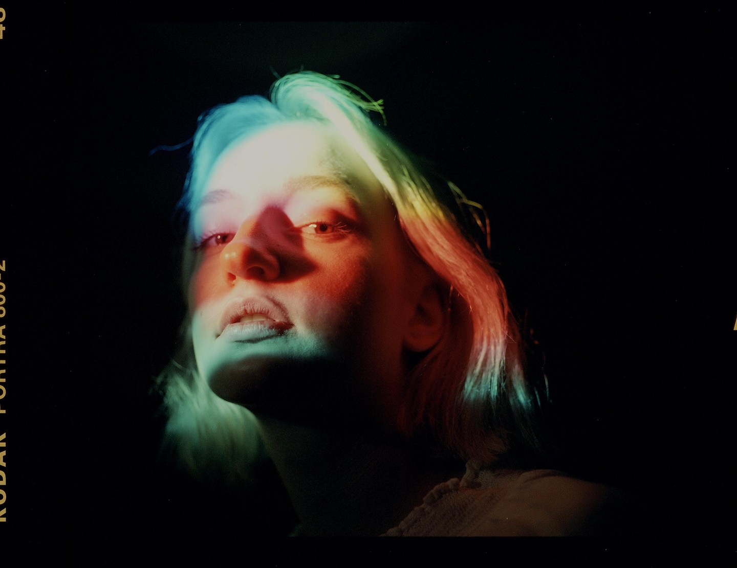 A woman's face is illuminated by colorful light in a dark setting.