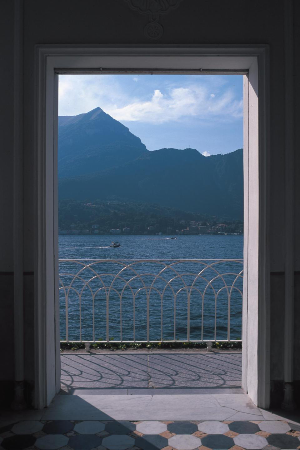 A view of a lake and mountains is framed by a doorway and a white railing.