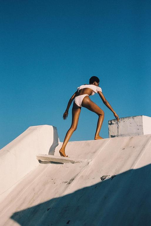 A woman in a bikini climbs a white roof against a clear blue sky.