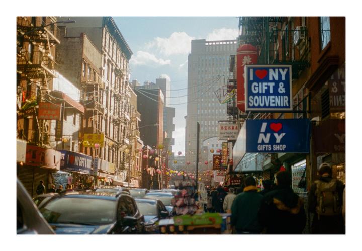 A busy street in Chinatown, New York City, is filled with cars, pedestrians, and shops with signs.
