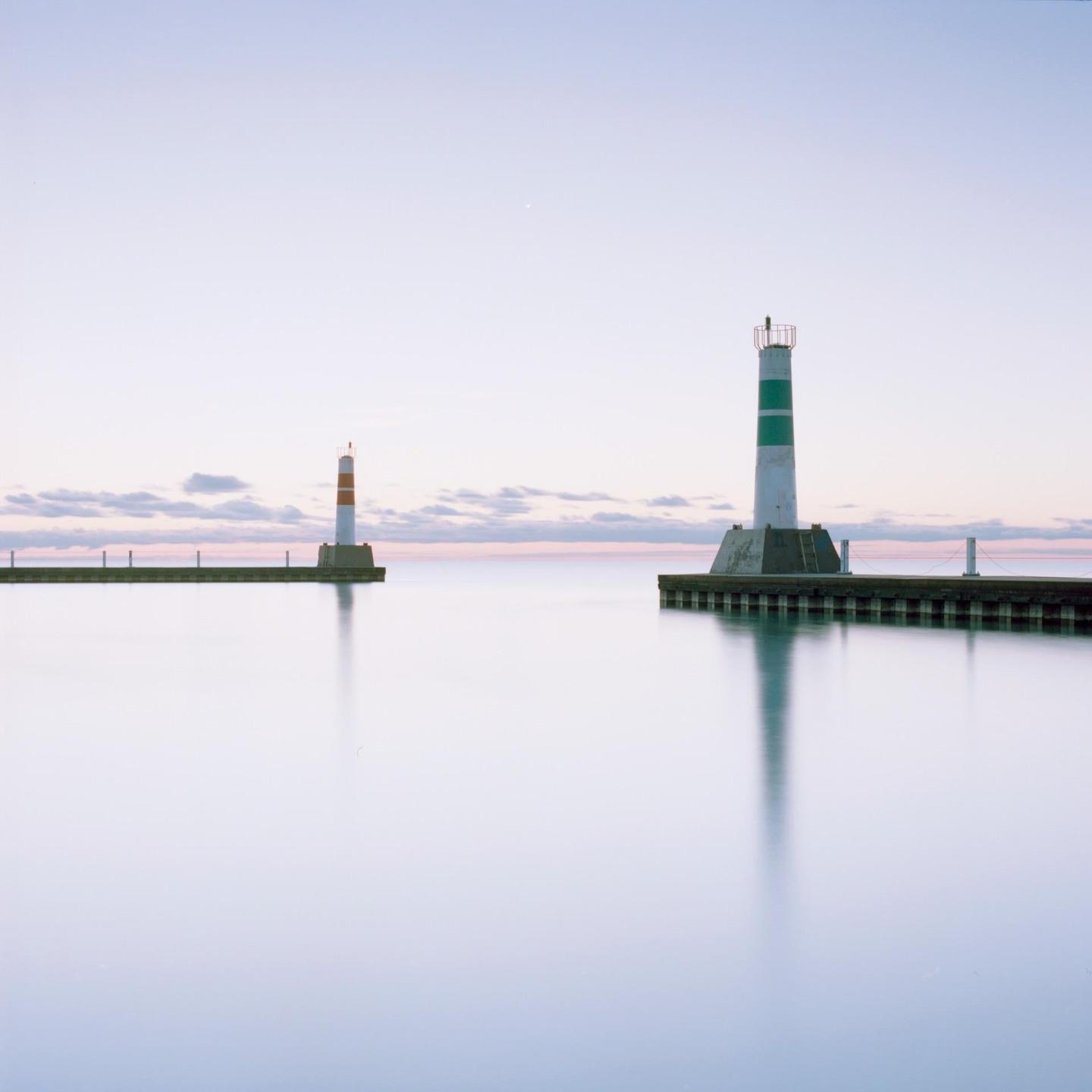 Two lighthouses stand on piers extending into calm water under a pale sky with a few clouds.
