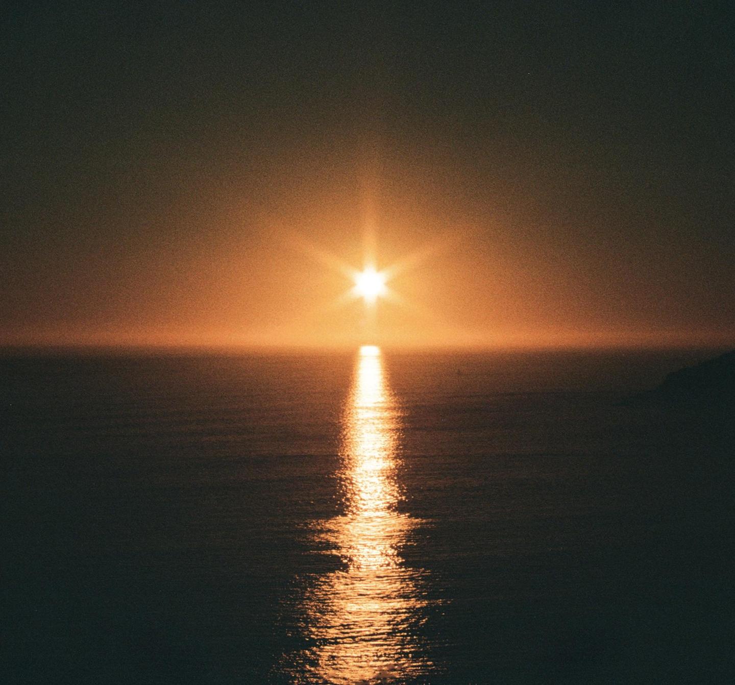 The sun sets over the ocean, creating a bright reflection on the water.