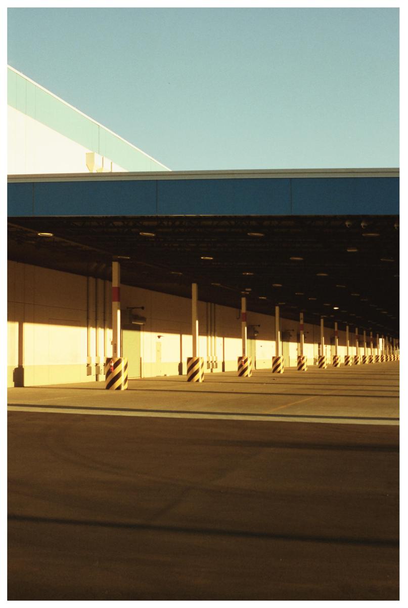 A long row of striped bollards stands in front of a building with a blue roof under a clear sky.