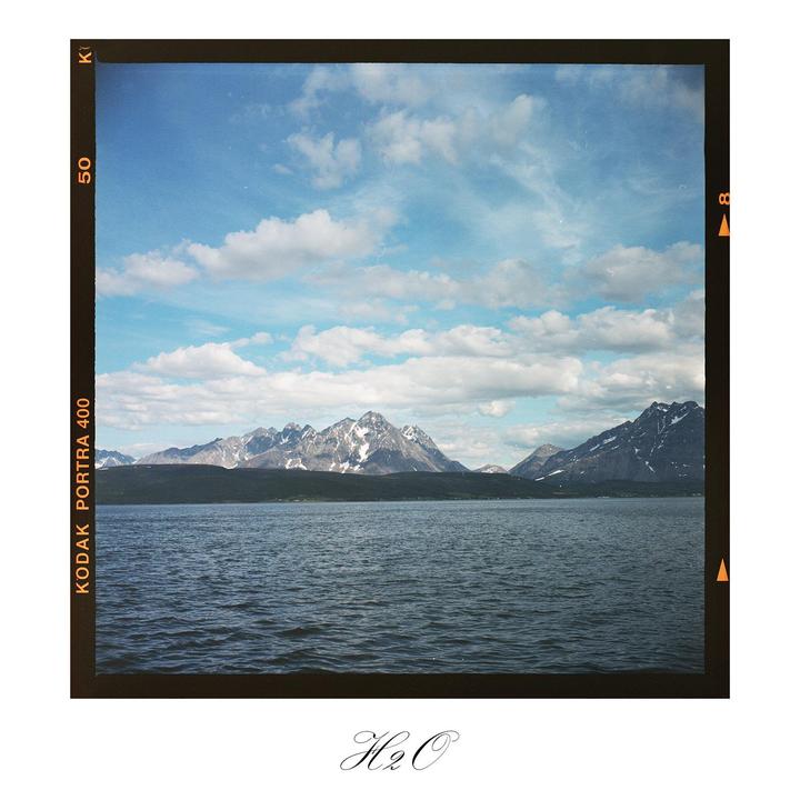 A body of water is in the foreground with snow-capped mountains and a cloudy sky in the background.