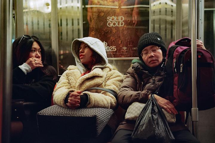 Three women are sitting on a subway train, one of whom is sleeping.