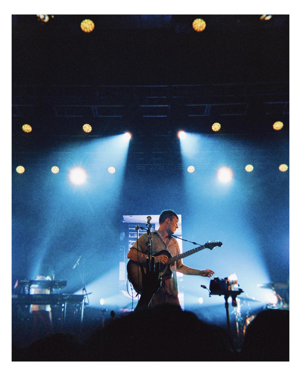 A man plays a guitar on a stage illuminated by blue spotlights.