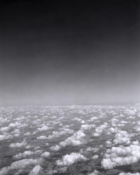 An aerial view shows a vast expanse of clouds floating above a patchwork of fields.