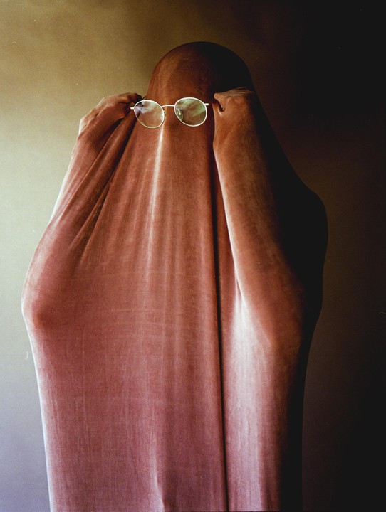 A person is covered by a pink fabric with only their hands and glasses visible.