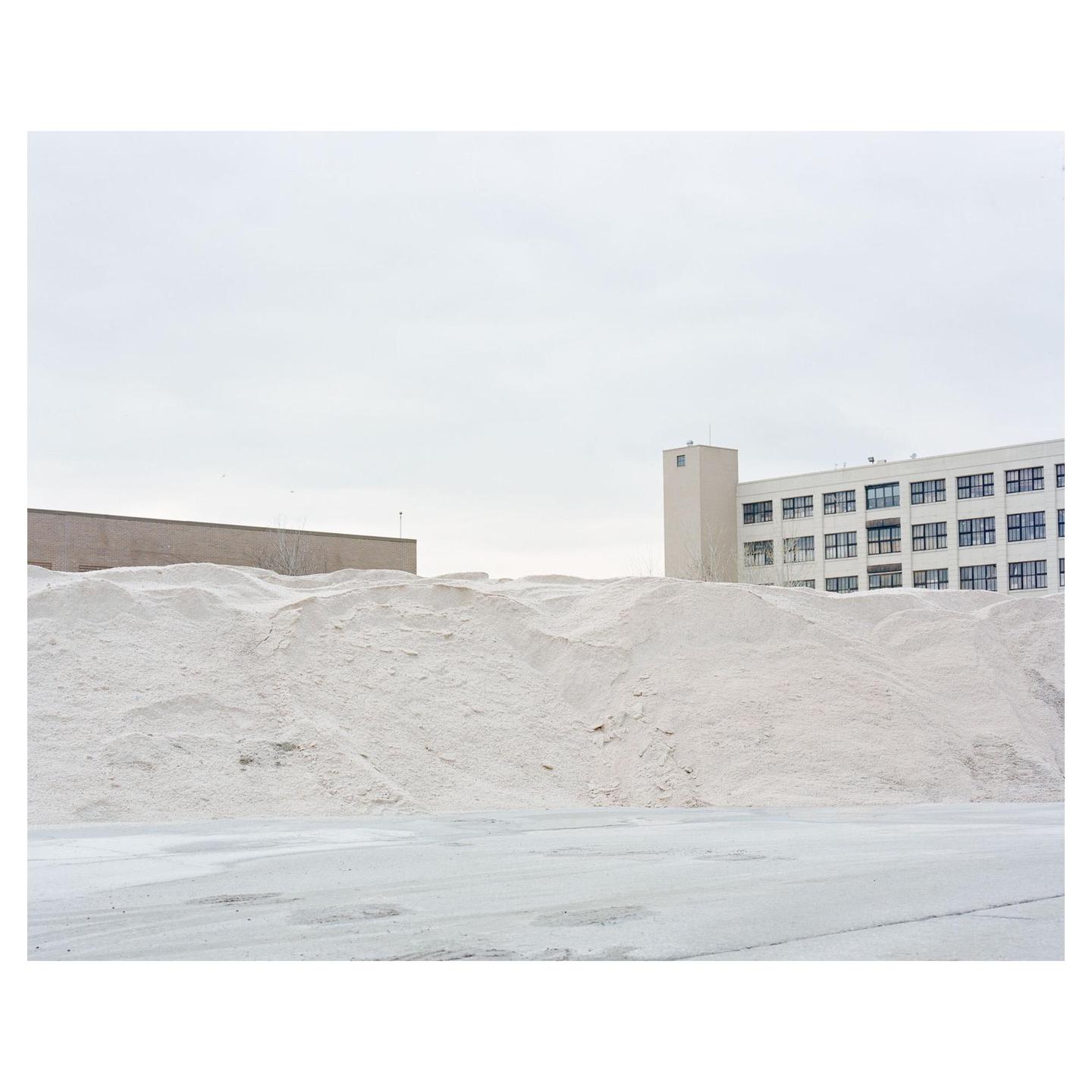 A large pile of white salt sits in front of two buildings under a cloudy sky.