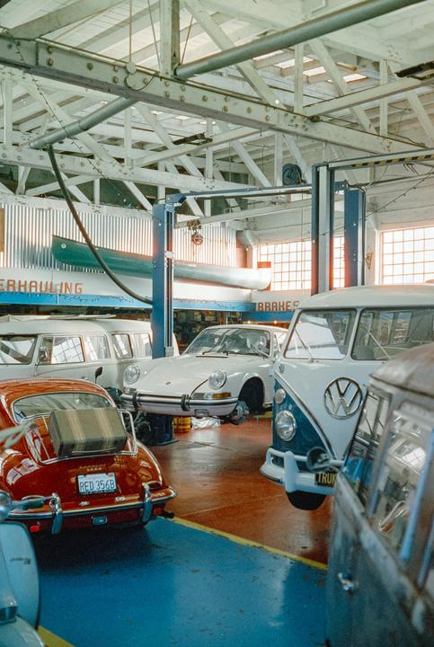 Several vintage vehicles are parked inside a garage with a canoe hanging from the ceiling.