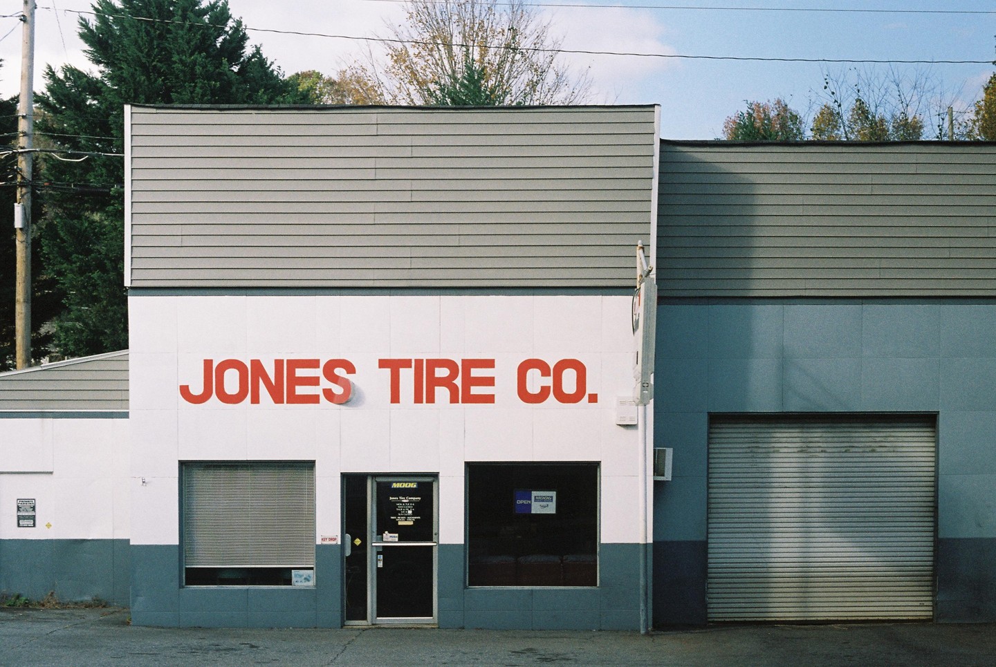 The exterior of a tire shop with red lettering on a white wall and a gray garage door.