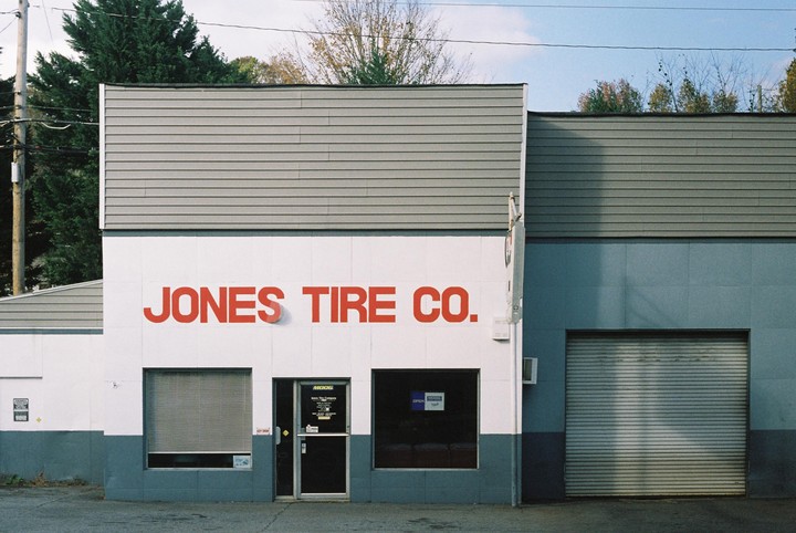 The exterior of a tire shop with red lettering on a white wall and a gray garage door.