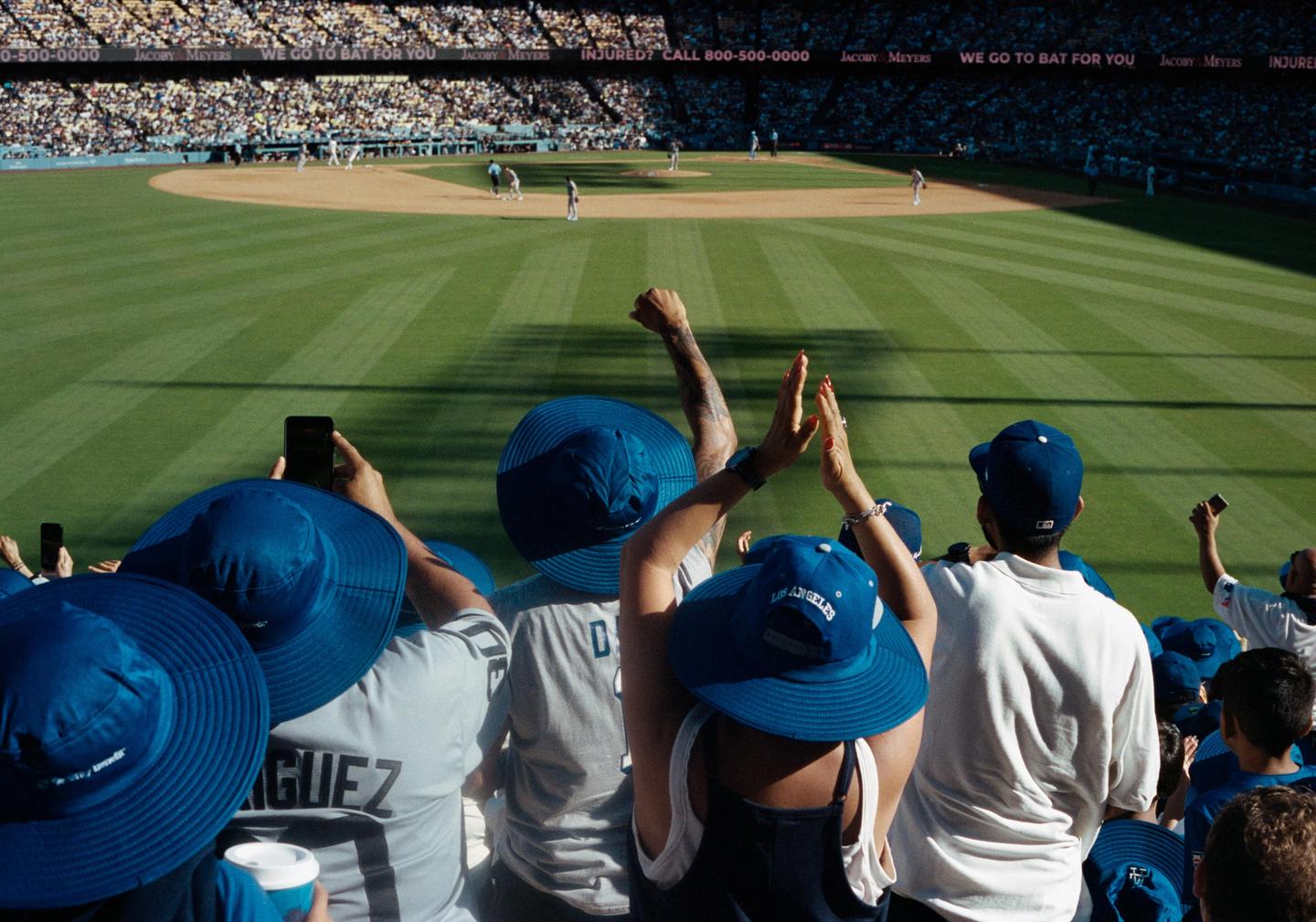 A crowd of people wearing blue hats watches a baseball game from the stands of Dodger Stadium.