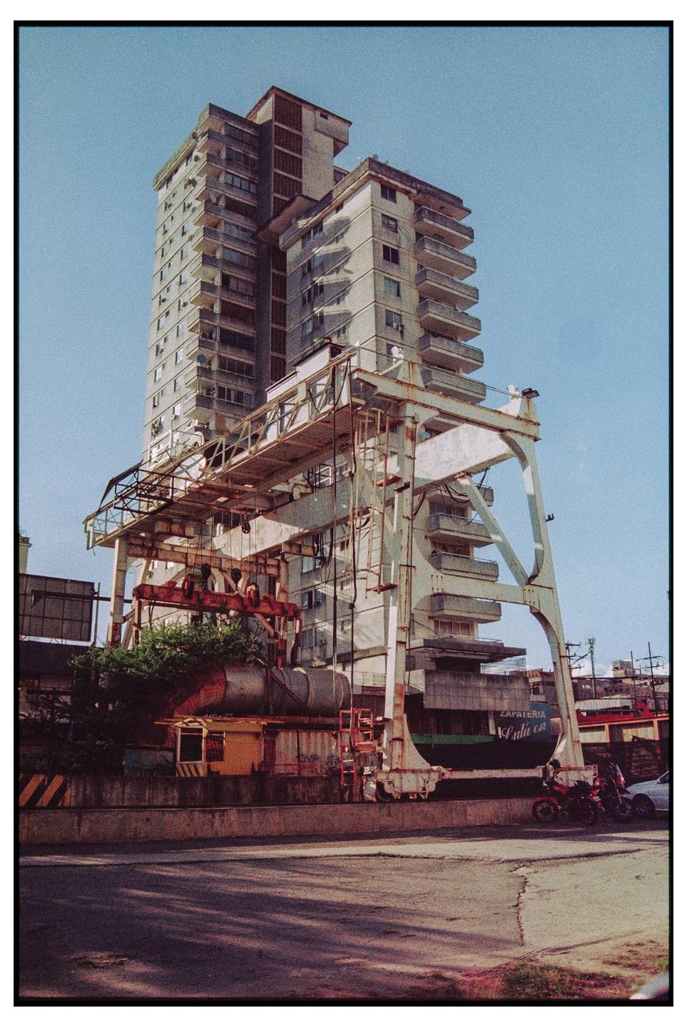 A tall building stands behind a large, rusty industrial crane next to a street.