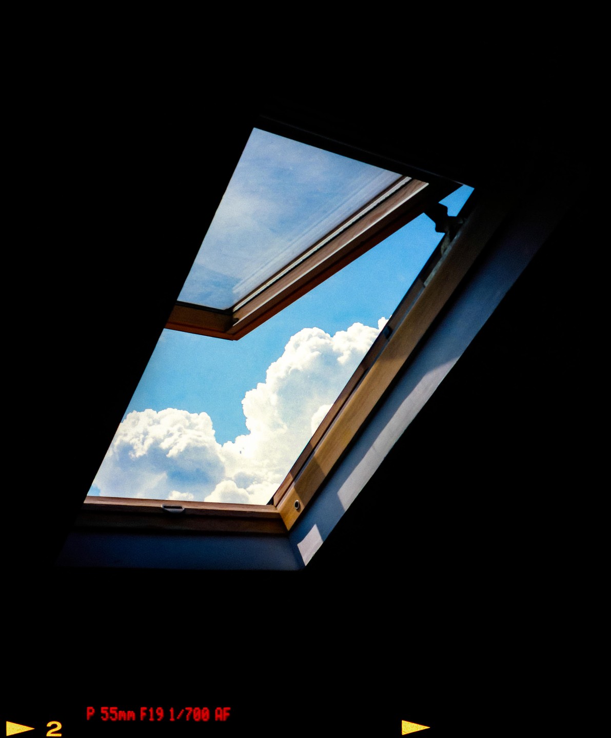 A bright blue sky with fluffy white clouds is visible through an open attic window.