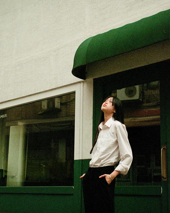 A woman stands with her head tilted back, looking up, next to a building with a green awning and trim.