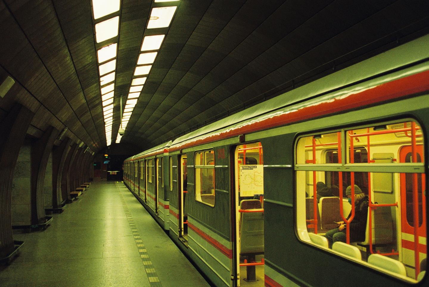 A subway train with open doors is stopped at a station platform with a person visible inside one of the cars.
