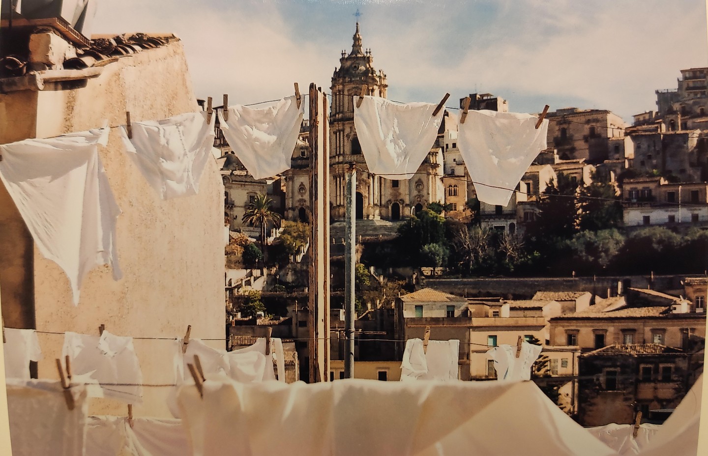 White laundry hangs on clotheslines in front of a hillside town with a large church.