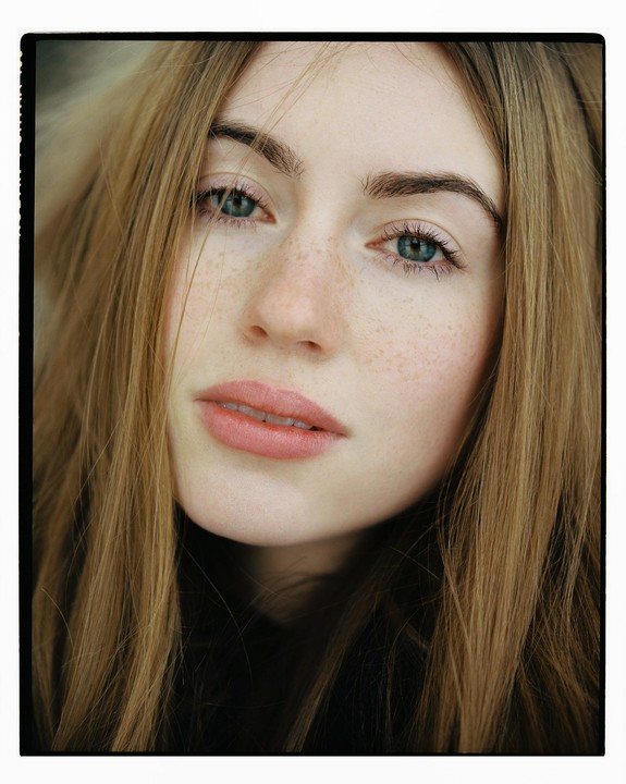 A woman with long hair and freckles looks directly at the viewer.