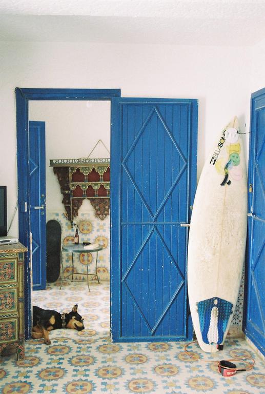 A dog sleeps on a patterned tile floor next to a surfboard and blue doors.
