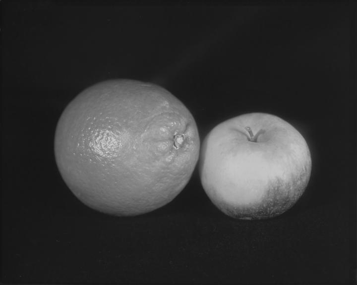An orange and an apple are side by side on a dark surface.