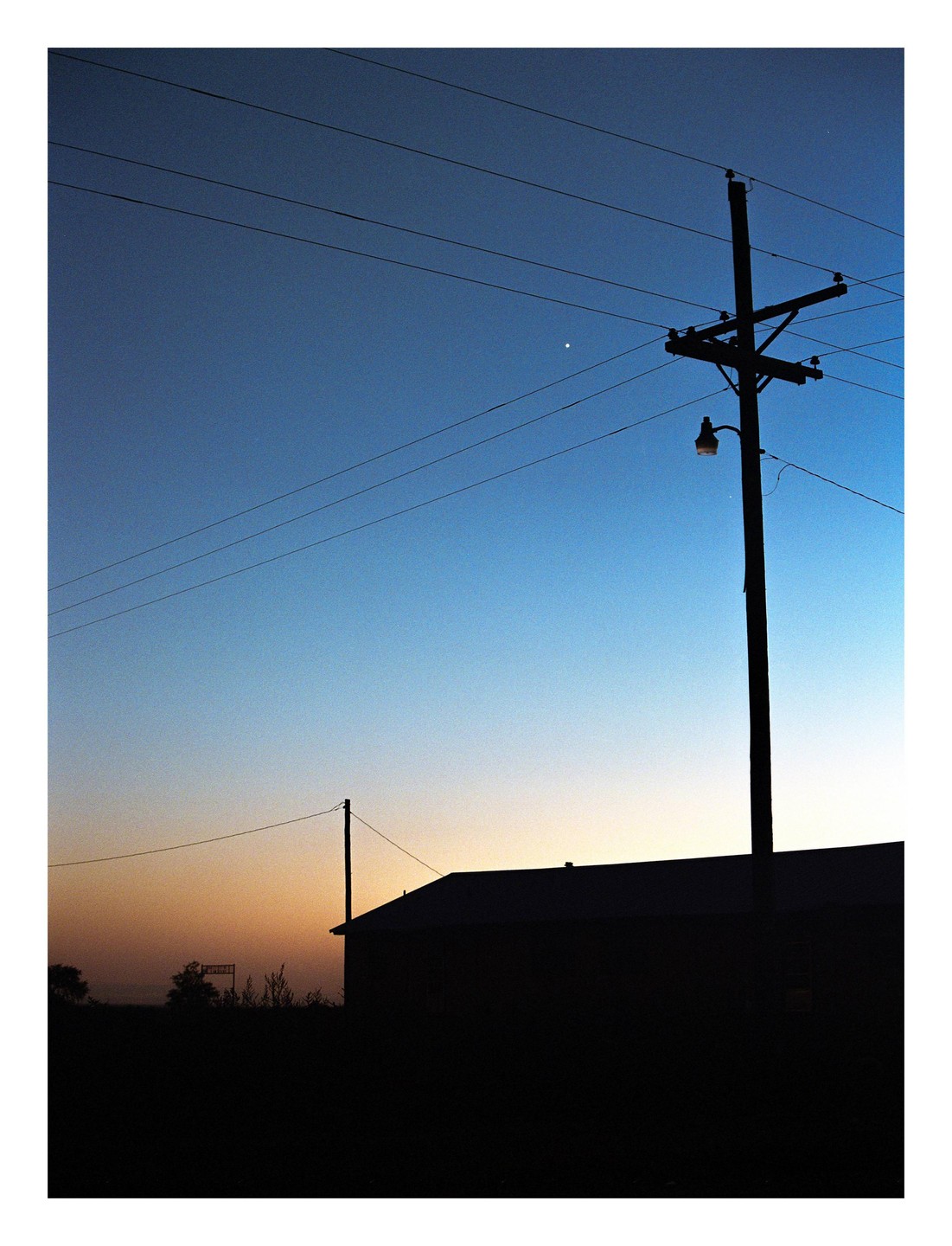 A utility pole and building are silhouetted against a gradient sky at dusk.