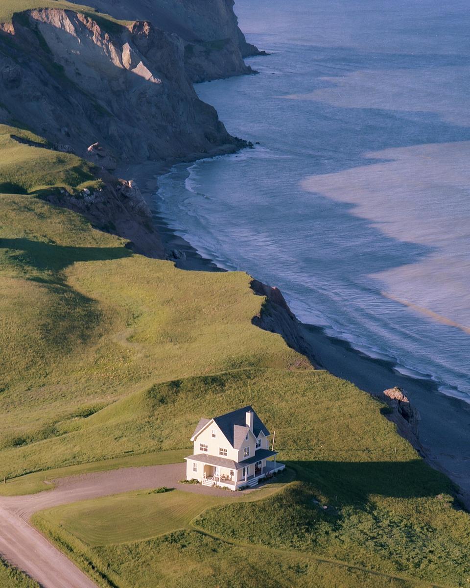 A house sits on a grassy cliff overlooking a beach and ocean.