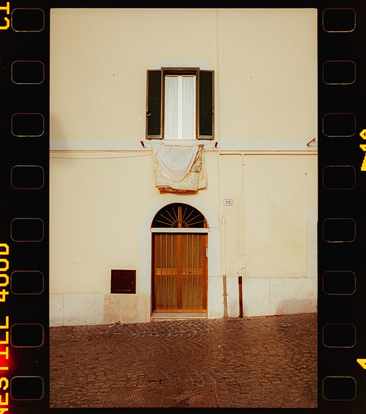 A building with a window, a door, and laundry hanging from a line is seen from a cobblestone street.