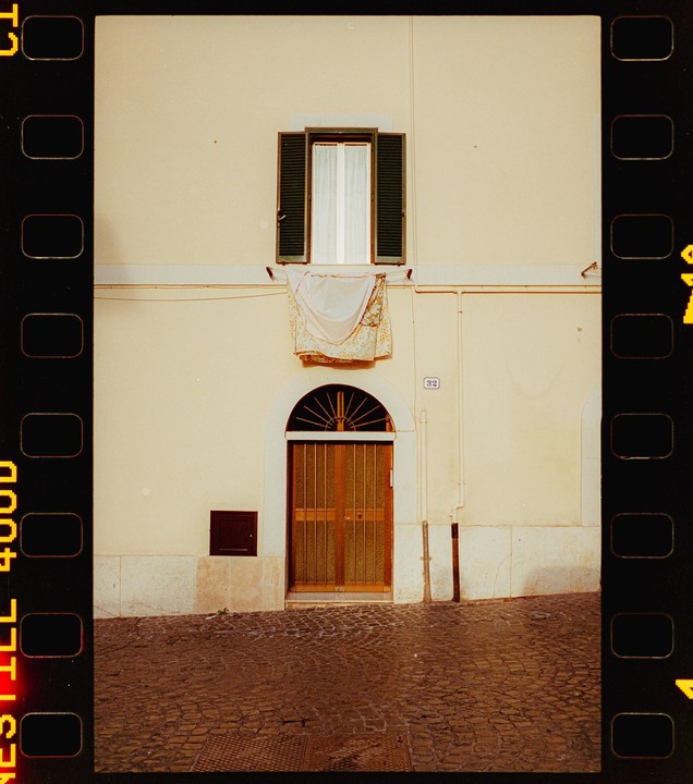 A building with a window, a door, and laundry hanging from a line is seen from a cobblestone street.