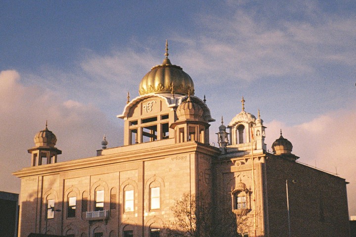 A large building with a golden dome and smaller domes is illuminated by warm sunlight under a partly cloudy sky.