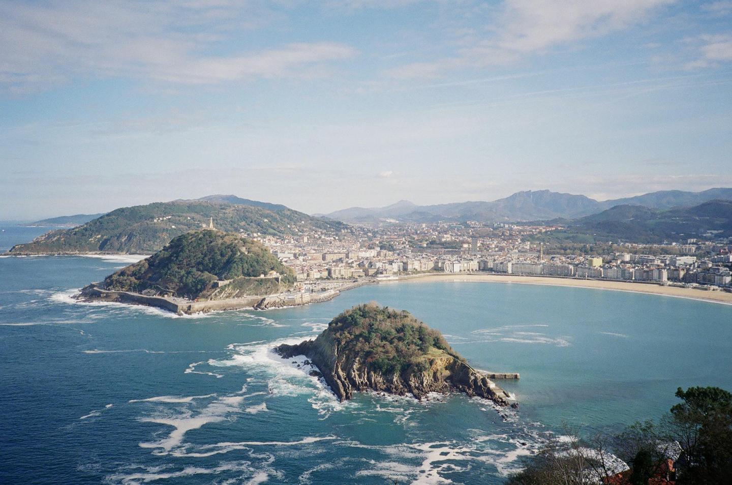 A panoramic view shows a bay with a city and mountains in the background, and two small islands in the foreground.