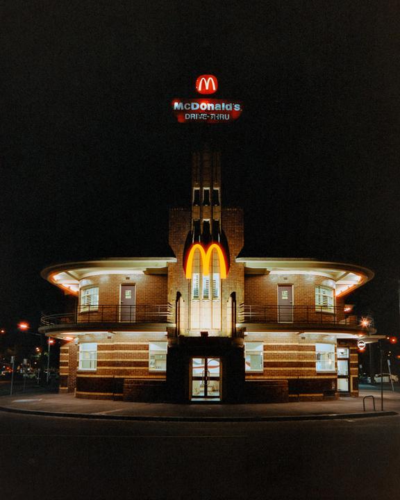 A McDonald's restaurant with a tall sign and glowing golden arches is illuminated at night.