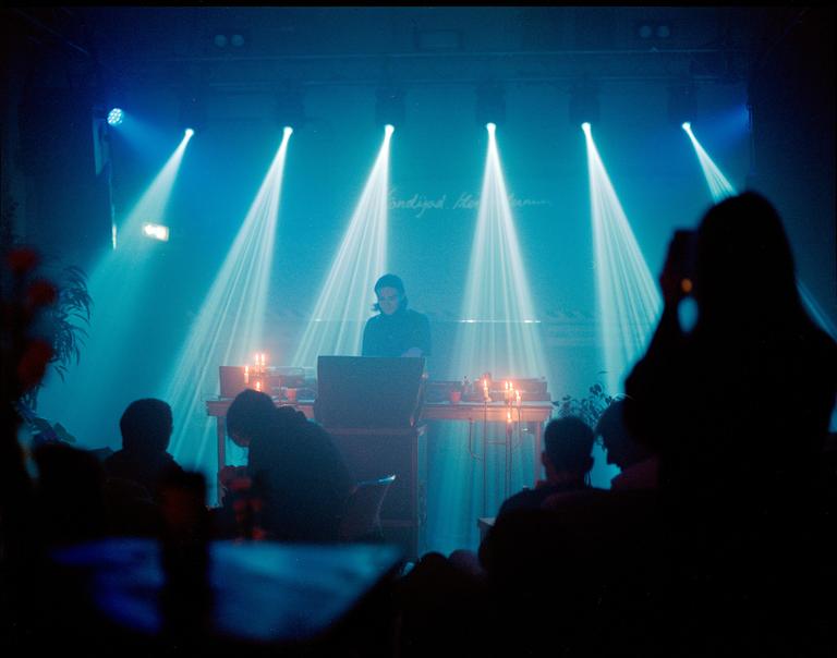 A musician performs on stage under blue spotlights while an audience watches.