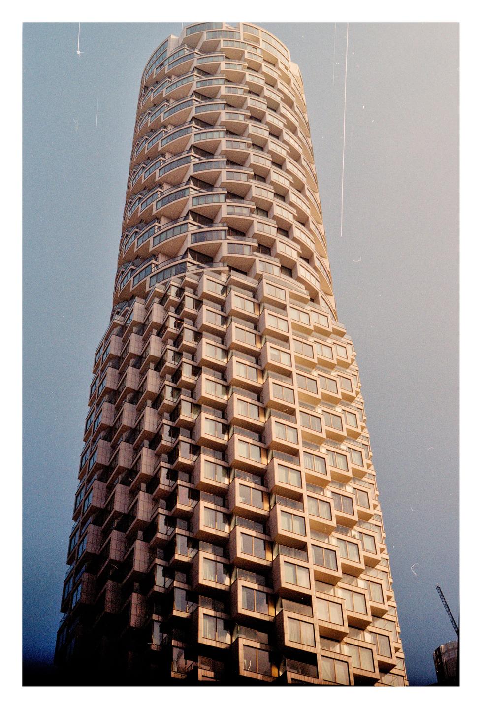 A tall, cylindrical building with many balconies and windows stands against a clear sky.