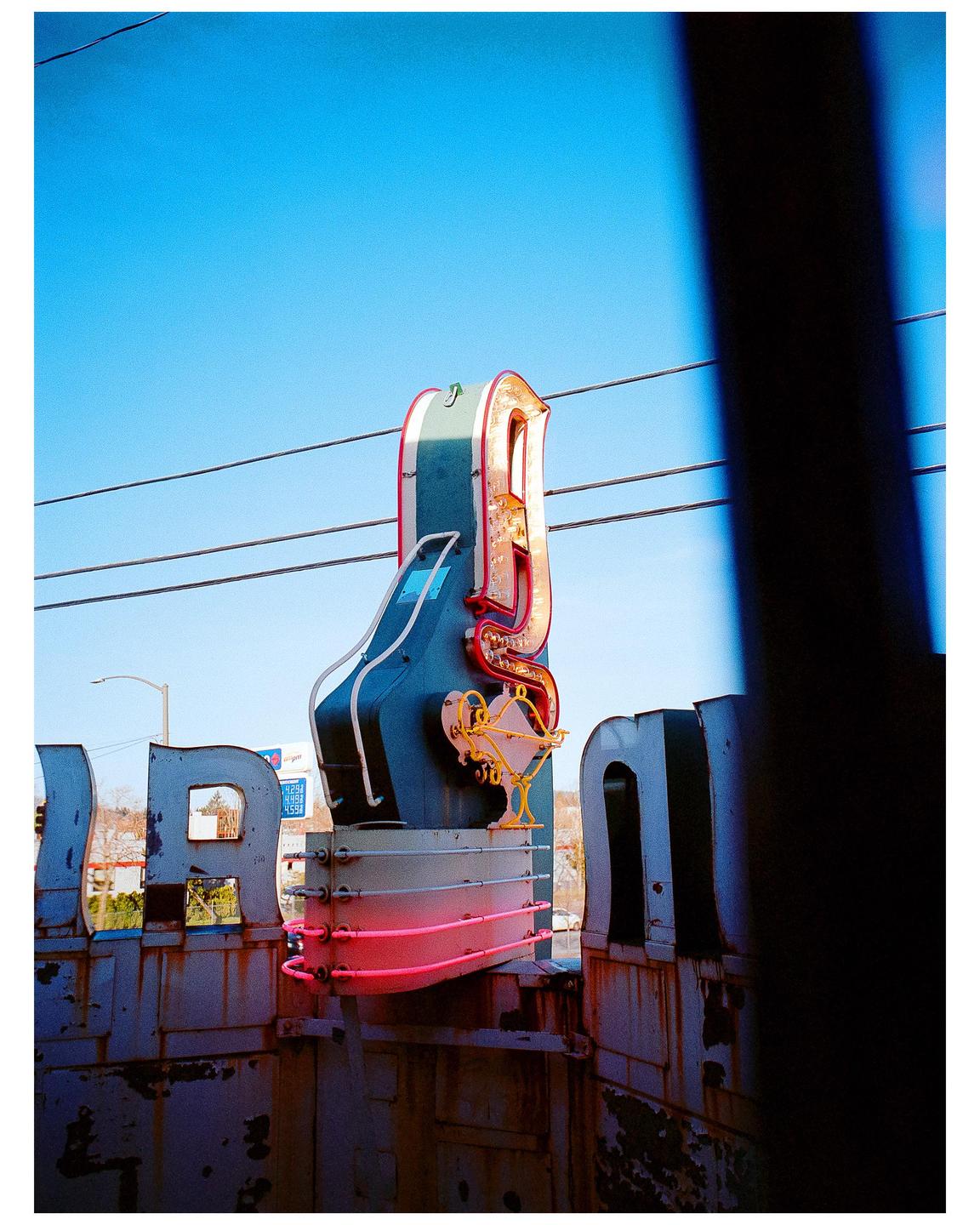 A neon sign with a martini glass is visible behind a rusty structure under a clear blue sky.