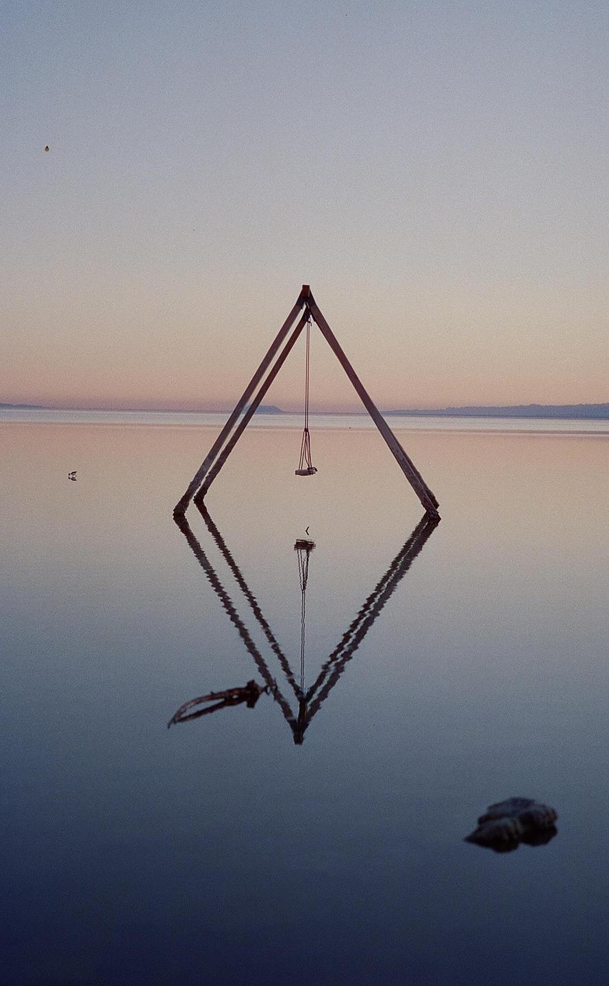 A swing set stands in the still water of the Salton Sea at dusk, with its reflection visible below.