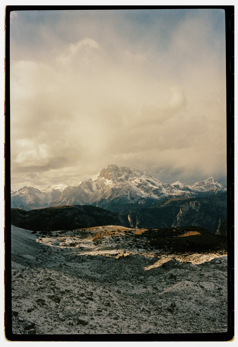 Snow-capped mountains rise above a rocky, snow-dusted landscape under a cloudy sky.